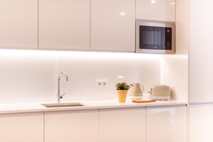 A modern kitchen with white cabinetry, a stainless steel microwave, a sink, and a toaster on the countertop.