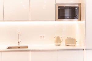 Eine moderne Küche mit weißen Schränken, einer Edelstahl-Mikrowelle, einem Wasserkocher und einem Toaster auf der Arbeitsfläche.