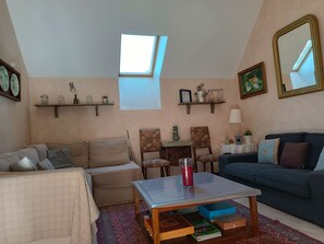 A cozy living room with a high ceiling, a skylight, and a mix of furniture including a sofa, a chair, and a coffee table.