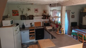 Cocina compacta con microondas, estufa y lavabo. Hay una zona de comedor con mesa y sillas.