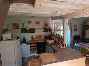 A compact kitchen with a microwave, stove, and sink. There is a dining area with a table and chairs.