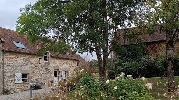 Un edificio de piedra con techo de tejas, un banco y un jardín con flores blancas.