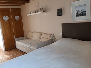 Une chambre à coucher comprenant un lit, un canapé, une armoire, une étagère avec des objets décoratifs et un tableau encadré accroché au mur.