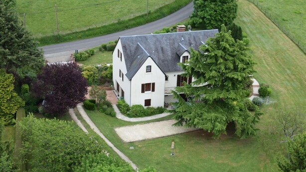 Ein weißes, zweistöckiges Haus mit geneigtem Dach, umgeben von üppiger Vegetation und einem gepflegten Rasen.