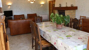 Ein Essbereich mit einem langen Tisch, Stühlen, einer Kühlpflanze, einem Kamin und einem Fernseher im Hintergrund.