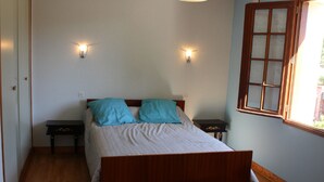 Ein Schlafzimmer mit einem hölzernen Bett, zwei Nachttischen, einem Fenster mit Holzrahmen und zwei Wandleuchten.