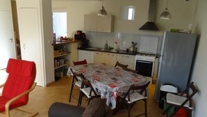 Ett kompakt kök med ett matbord, stolar, en röd stol, en soffa och ett kylskåp.