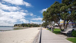 A beach with a wooden boardwalk, benches, and trees. - Sunshine Daydream w Edmund Cottage (Auckland)