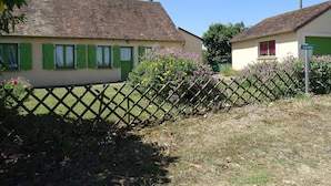 Une maison de campagne avec un toit en tuiles, des volets verts et une clôture en bois.