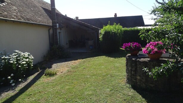 Il s’agit d’une propriété résidentielle dotée d’une allée pavée, d’un petit jardin devant la maison agrémenté de fleurs blanches et d’un mur en pierre orné de fleurs roses.