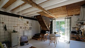 A spacious living room with a high ceiling, a staircase, and a kitchen area with a view of the outdoors.