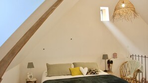 A cozy bedroom with a sloped ceiling, a bed with a dark green blanket, and a hanging light fixture.