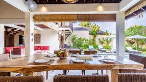 A dining area with a large wooden table, wicker chairs, and a view of the outdoor garden and pool. - Pristine Villa Yuyu Balian (Tabanan)