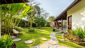A well-maintained garden with a stone pathway leading to a building with a wooden roof. - Pristine Villa Yuyu Balian (Tabanan)