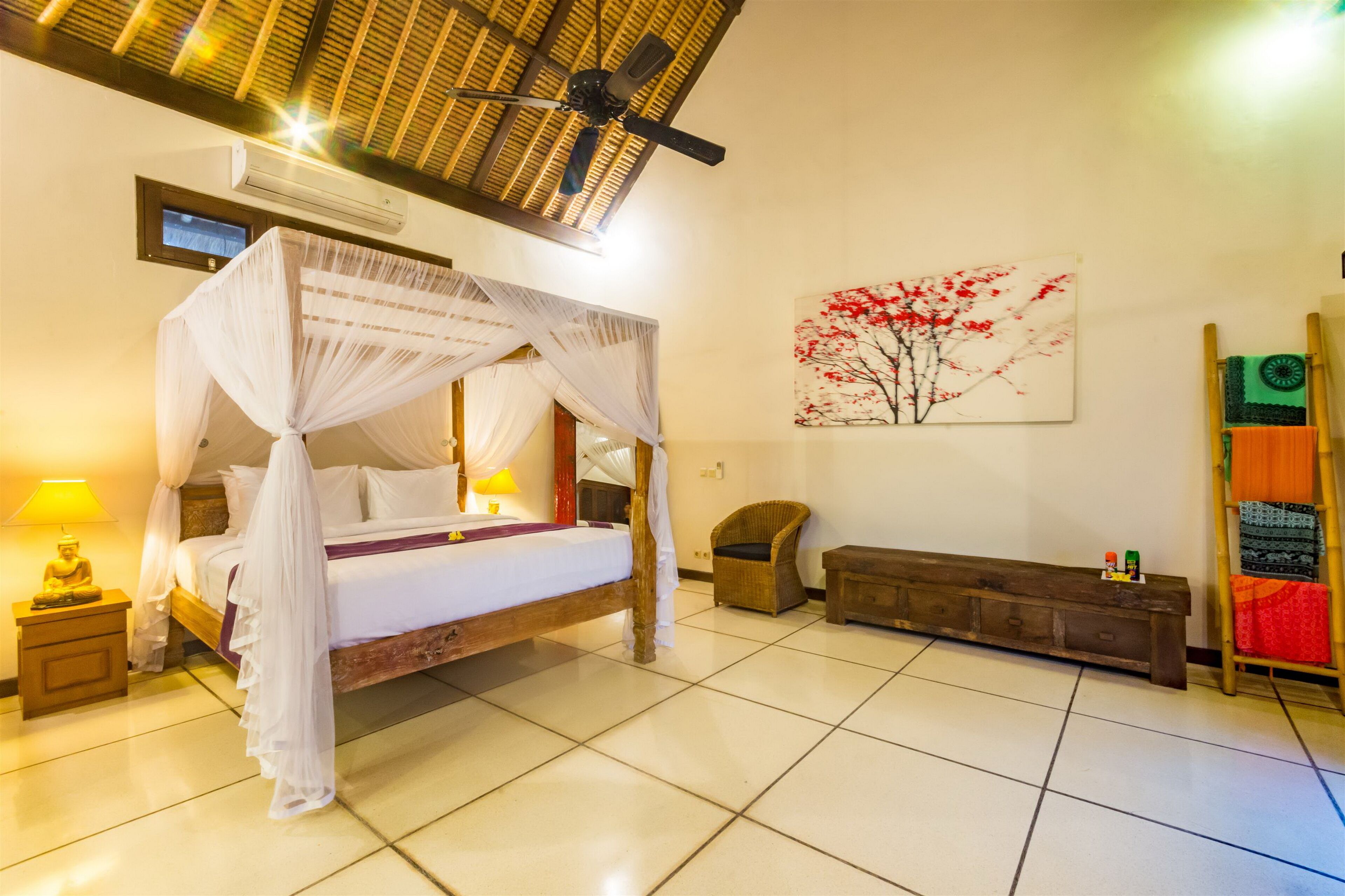 A bedroom with a four-poster bed, a wooden bench, a wall-mounted air conditioner, and a ceiling fan.