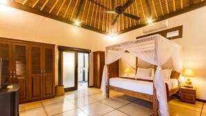 Une chambre d’hôtel avec un lit à baldaquin, un ventilateur de plafond, une table de chevet avec une lampe et une armoire.