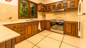 A kitchen with wooden cabinets, a stainless steel stove, and a refrigerator. - Villa Arjuna (Seminyak)
