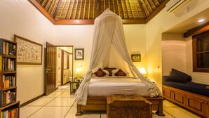 A room with a four-poster bed, a wooden bookshelf, a nightstand, and a sofa. - Villa Arjuna (Seminyak)