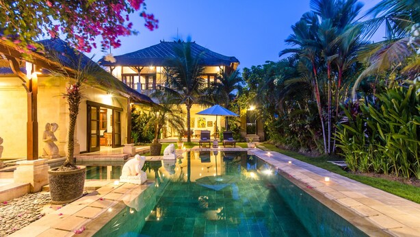 A luxurious pool area with a clear view of the pool, lounge chairs, and a well-lit building in the background. - Villa Arjuna (Seminyak)