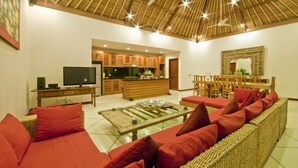 Ein geräumiges Wohnzimmer mit einer großen Couch, einem Couchtisch und einem Fernseher. Es gibt eine Küchenzeile mit Holzausbau und einen Esstisch mit Stühlen.