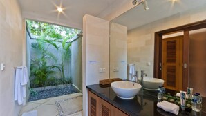 Ein modernes Badezimmer mit großem Spiegel, einem weißen Waschbecken und einer Duschkabine mit Blick auf Grünflächen.