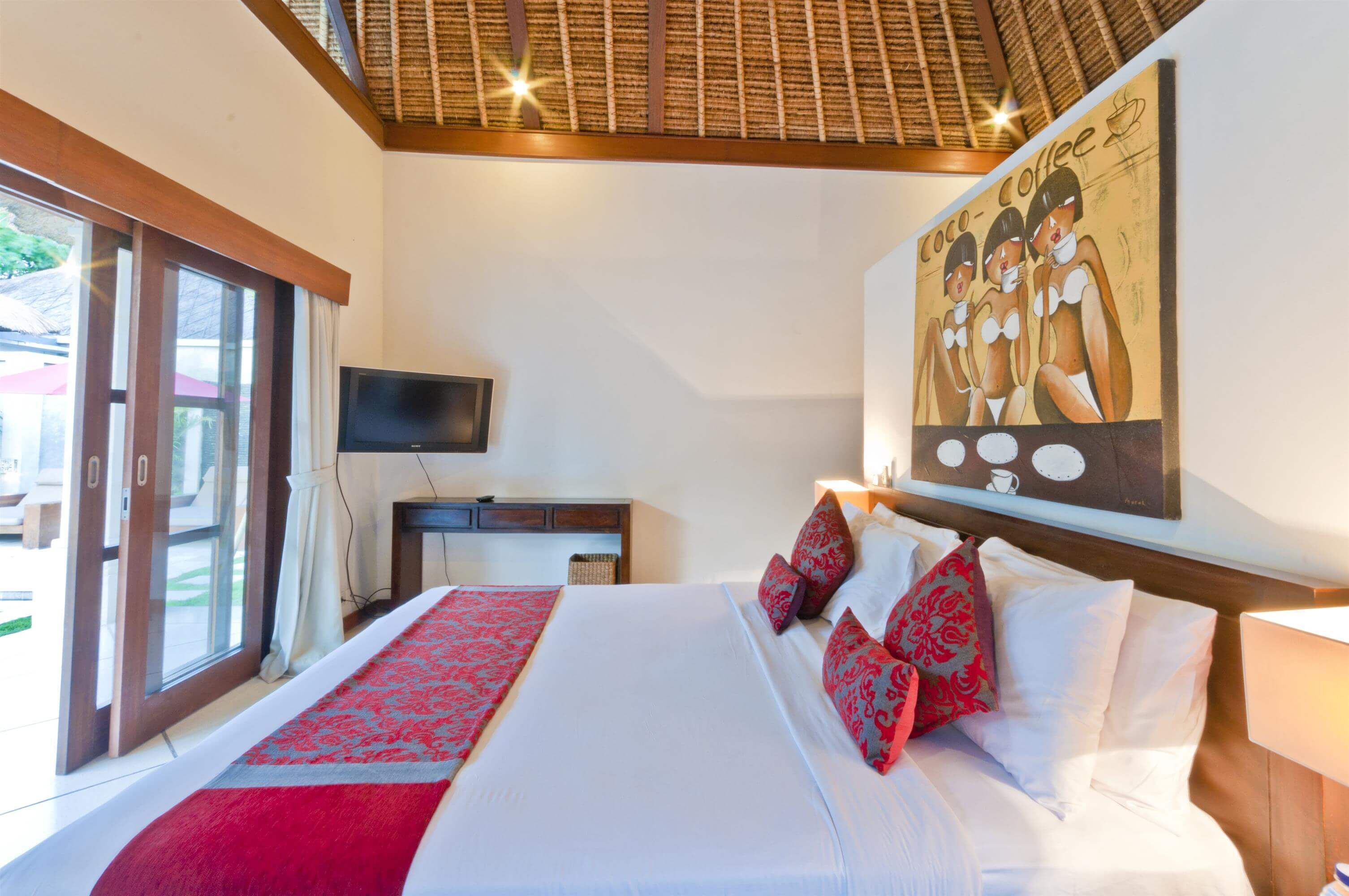 Habitación de hotel con una cama grande, un televisor, un cuadro en la pared y vistas a través de la puerta de vidrio.