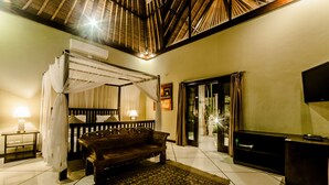 A room with a wooden bench, a patterned rug, an air conditioning unit, a television, and a large window with curtains. - Villa Kebun (Seminyak)