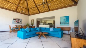 A spacious living area with a large blue sectional sofa, a round coffee table, and a dining set. - Villa Alore (Seminyak)