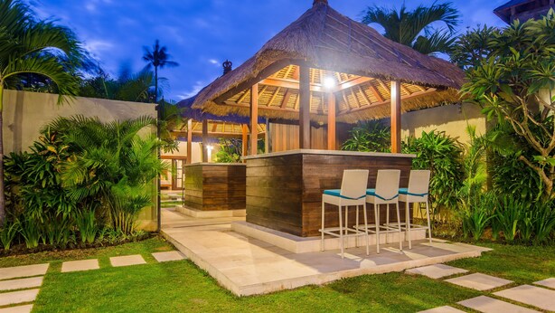 A thatched-roof gazebo with a wooden table and chairs, surrounded by lush greenery and a well-maintained lawn. - Villa Alore (Seminyak)