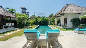 A swimming pool with lounge chairs and a thatched-roof building. - Villa Alore (Seminyak)