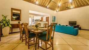 A spacious living area with a high ceiling, a dining table set for four, a blue sofa, and a television. - Villa Alore (Seminyak)