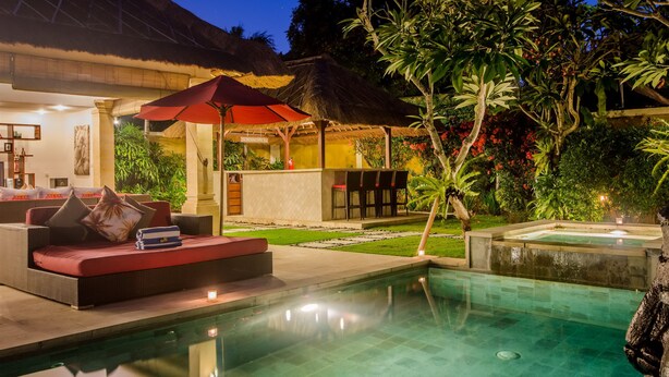 An outdoor pool area with a thatched-roof structure, seating, and lush greenery. - Villa Jaclan (Seminyak)