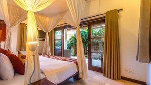 A bedroom with a canopy bed, a bedside table, and a view of the outdoors through a sliding glass door. - Villa Jaclan (Seminyak)