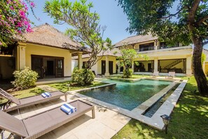 A poolside area with lounge chairs, a swimming pool, and a building with a thatched roof.