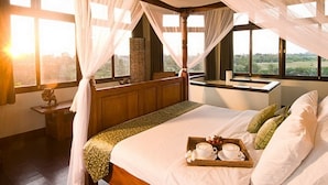 A bedroom with a large bed, a bedside table, a window with a view of greenery, and a canopy bed.