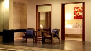Una habitación de hotel con una cama, dos sillones de mimbre, una mesita y un espejo.