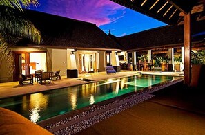A poolside area with a thatched-roof structure, lounge chairs, and a clear pool.