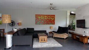 A modern living room with a grey sofa, a black armchair, a wooden coffee table, a floor lamp, a painting, and a television. - Villa Padar (Kerobokan)