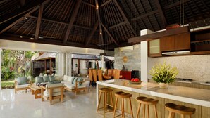 Un salón comedor amplio con techo alto, vigas de madera, una isla grande con taburetes y vista al exterior.