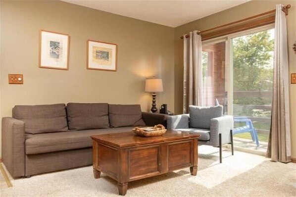 A living room with a brown sofa, a wooden coffee table, and a blue armchair. There are two framed pictures on the wall and a lamp on a side table. - TMD202-Cozy Condo located in Timberline! (Davis)