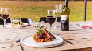 Een bord steak met groenten op een houten tafel, omringd door wijnglazen en flessen.
