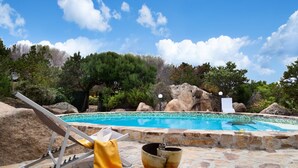 A stone pool with a clear blue sky, surrounded by rocks and trees.