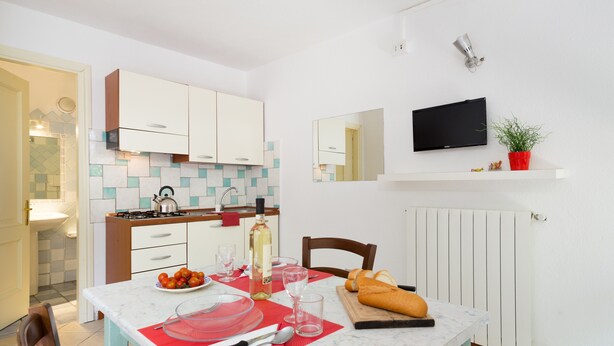 A modern kitchen with white cabinets, a tiled backsplash, a dining table set with plates, glasses, and a bottle.