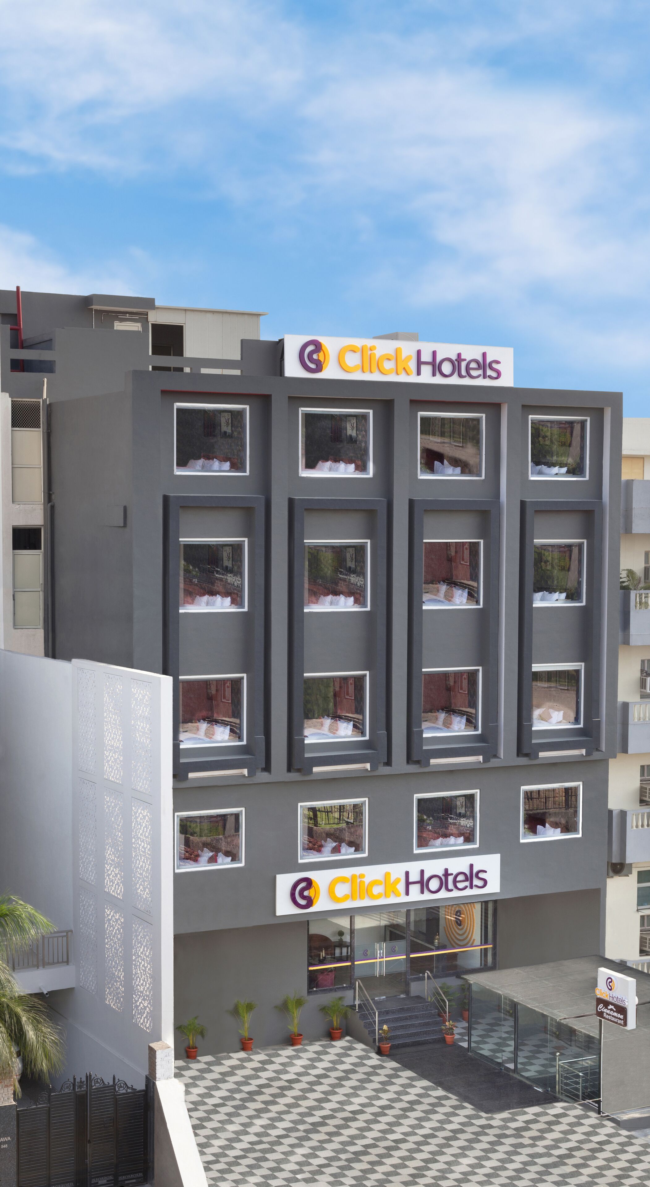 Edificio de Click Hotels con varios balcones, piso a cuadros y plantas en macetas en la entrada.