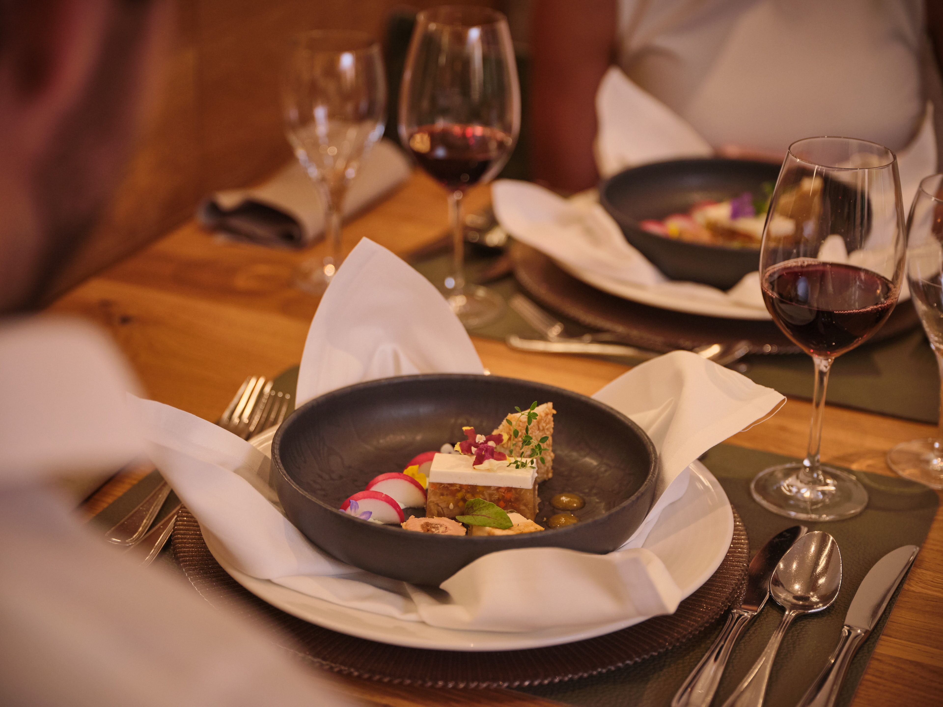 A dining table with a plate of food, a glass of red wine, and cutlery.