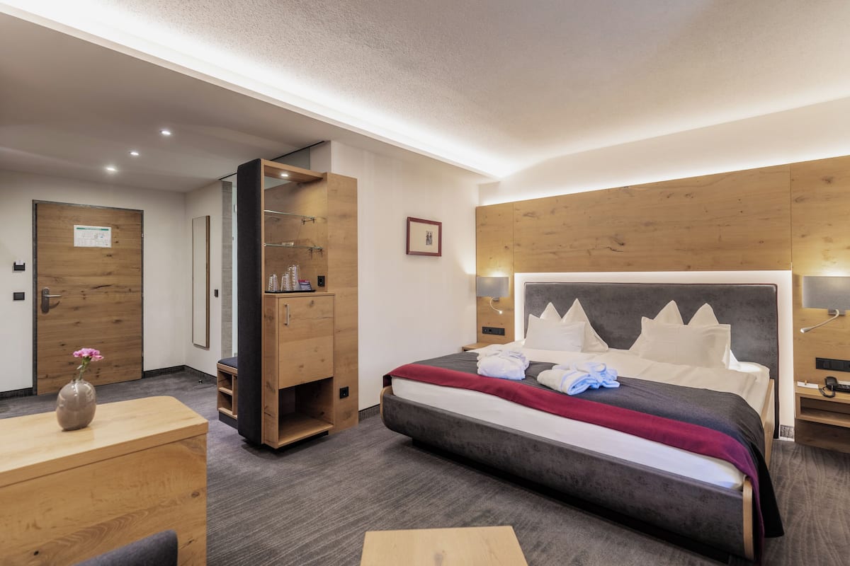 A modern hotel room with a large bed, wooden wardrobe, and a desk with a vase.