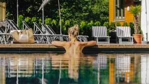A person relaxing by a pool with lounge chairs and umbrellas in the background. - Sporthotel Wagrain (Wagrain)