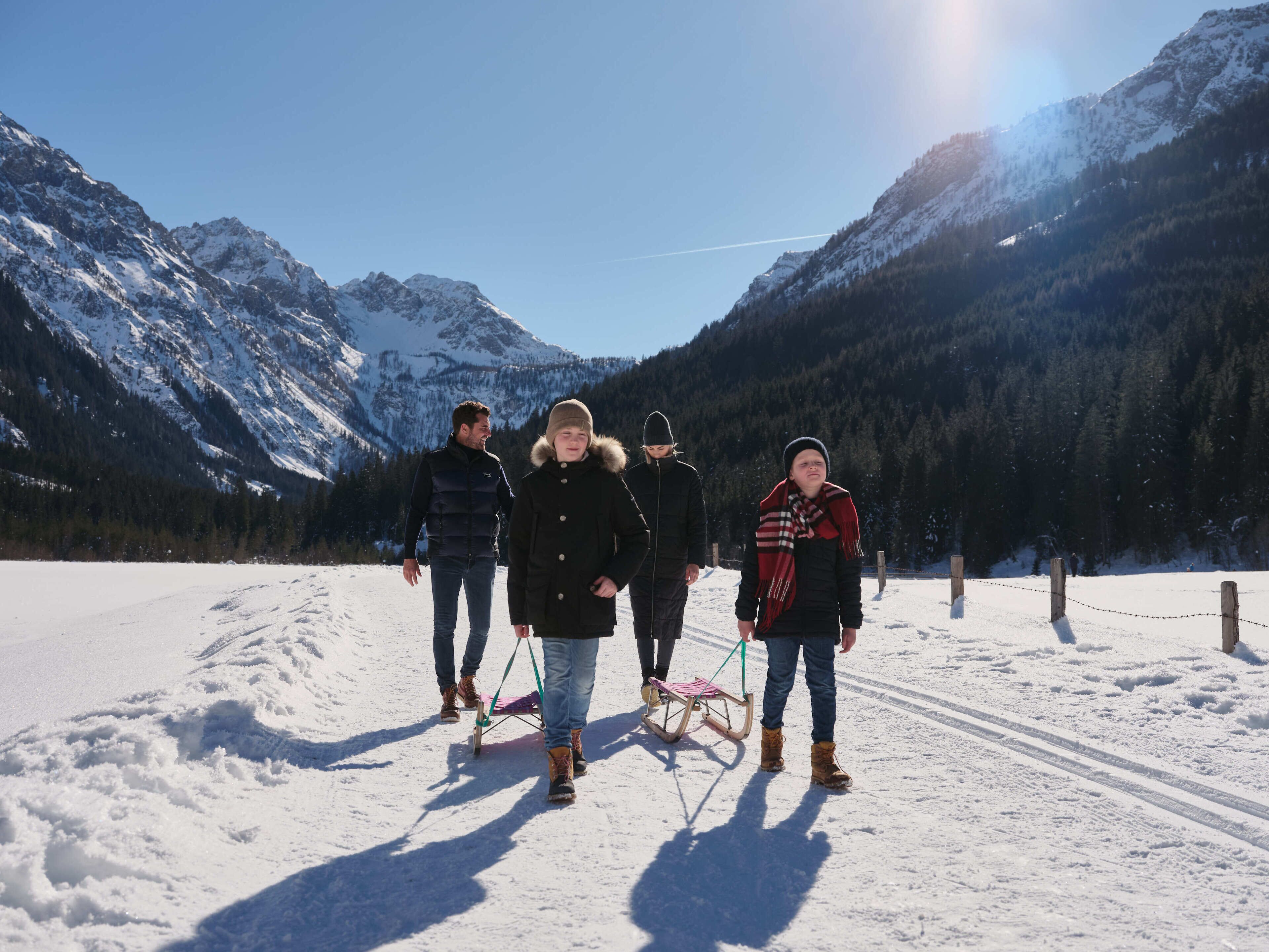A group of people walking on a snow-covered path with mountains in the background.