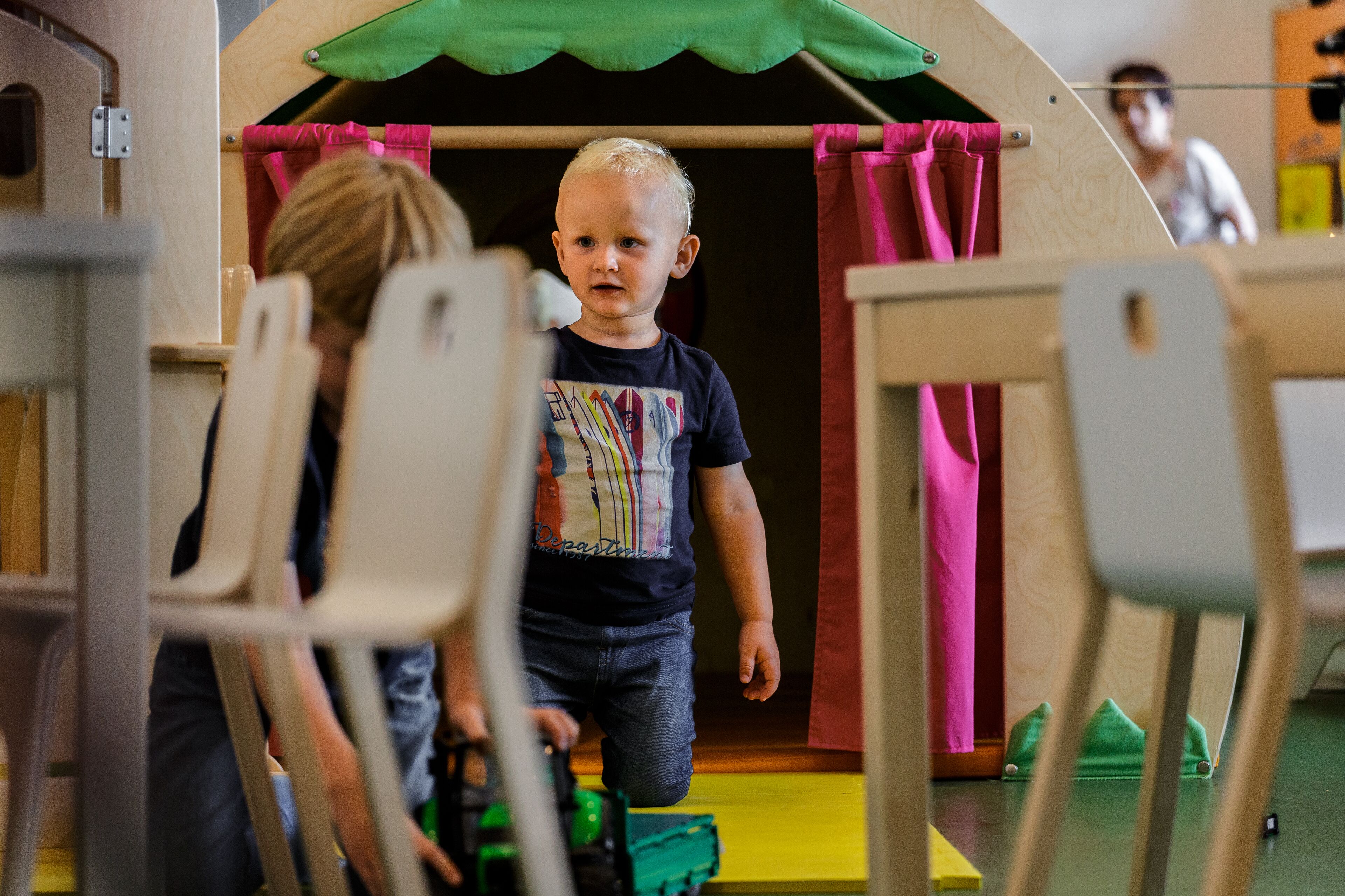 Un niño caminando hacia una casita de juegos con techo verde y cortinas rosas.