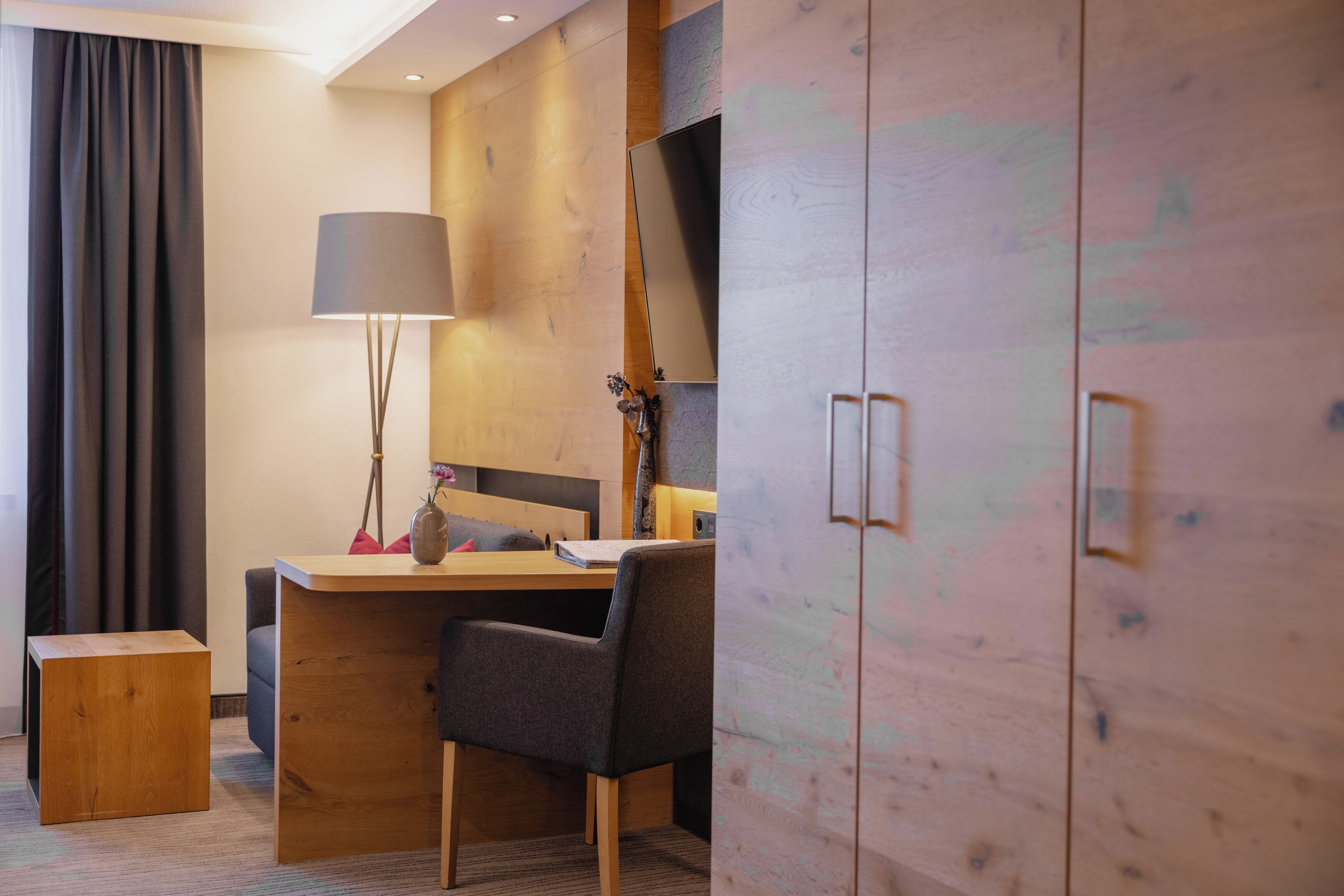 Een moderne hotelkamer met een houten bureau, een stoel, een lamp en een kledingkast.